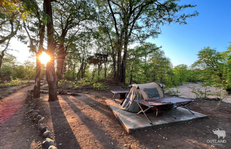 Wilderness camping in a tent with stretchers in Botswana with the sun setting behind beautiful trees - Outland Tavel