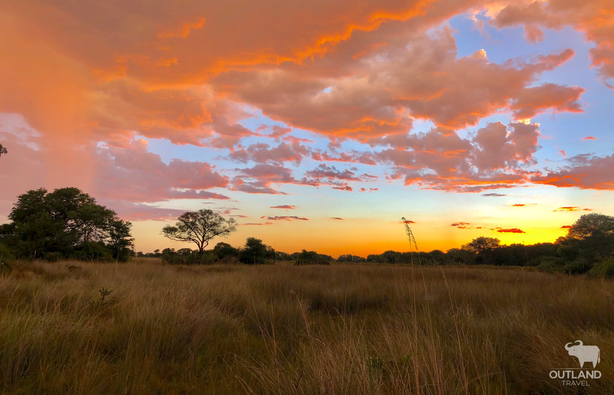 Beautiful orange and pink African sunset setting over the grasslands and savanna - Outland Travel