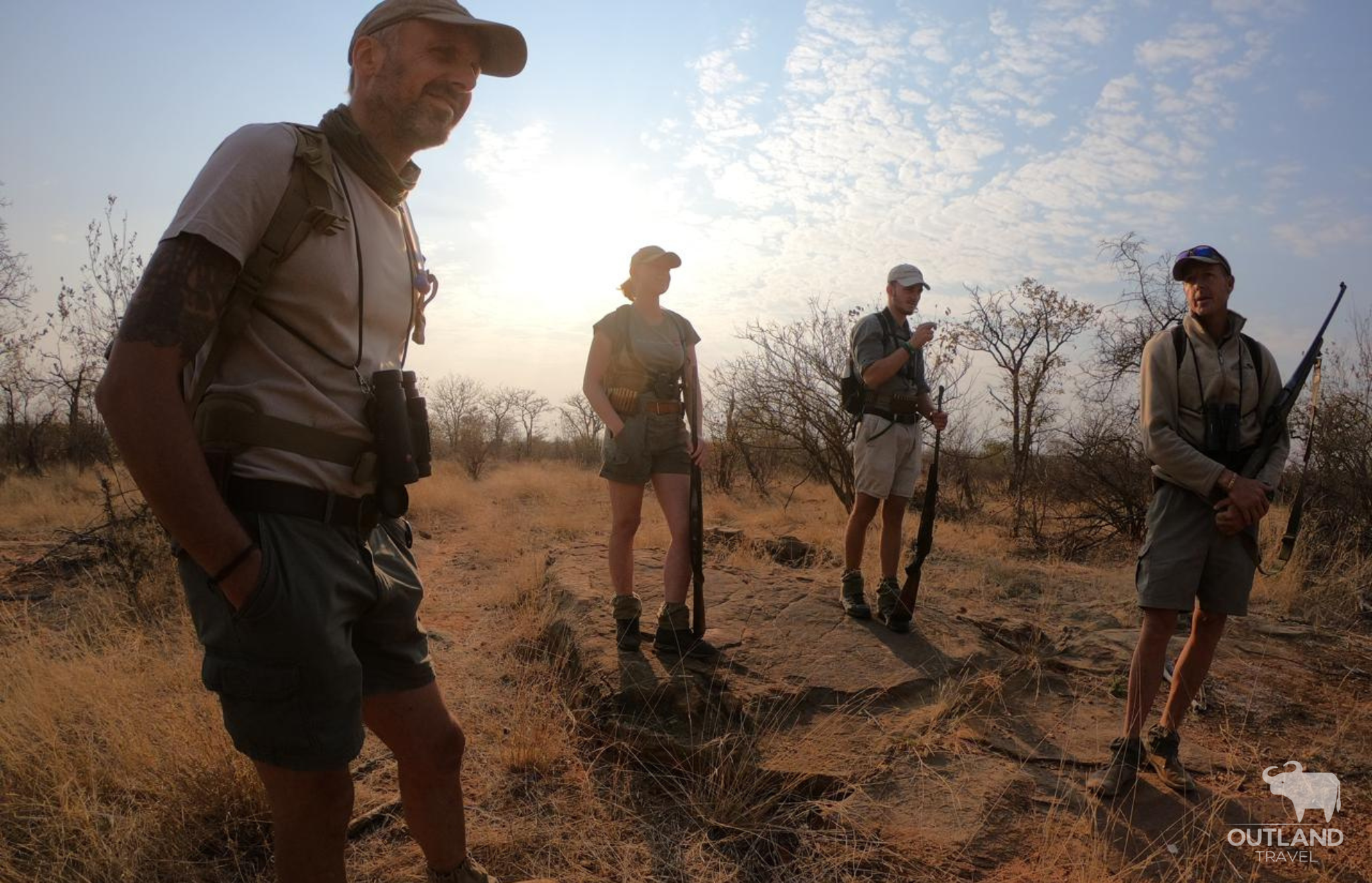 Walking safari with armed safari guides with the sun setting behind them - Outland Travel